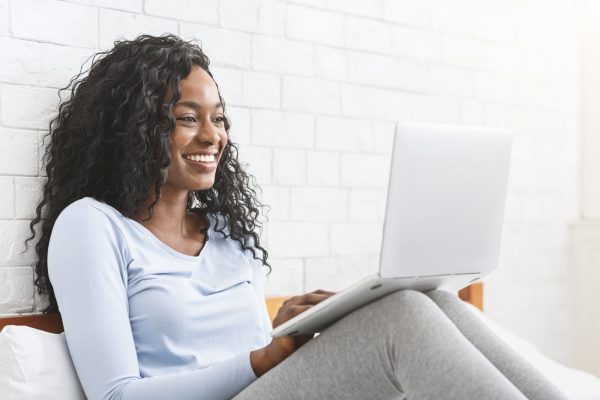 Happy young afro lady chatting online in bedroom